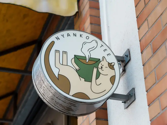 Rundes Aushängeschild von Nyanko Tee mit Katzen-Illustration an der Hauswand.