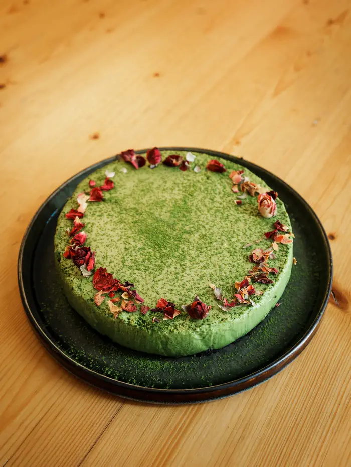 Ganze Matcha-Torte mit essbaren Blütenblättern am Rand.